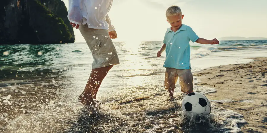 Man and child playing soccer in the water at a beach