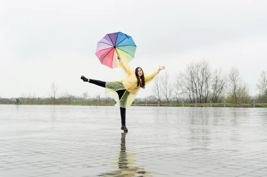 woman with yellow raincoat and colorful umbrella dancing in the rain