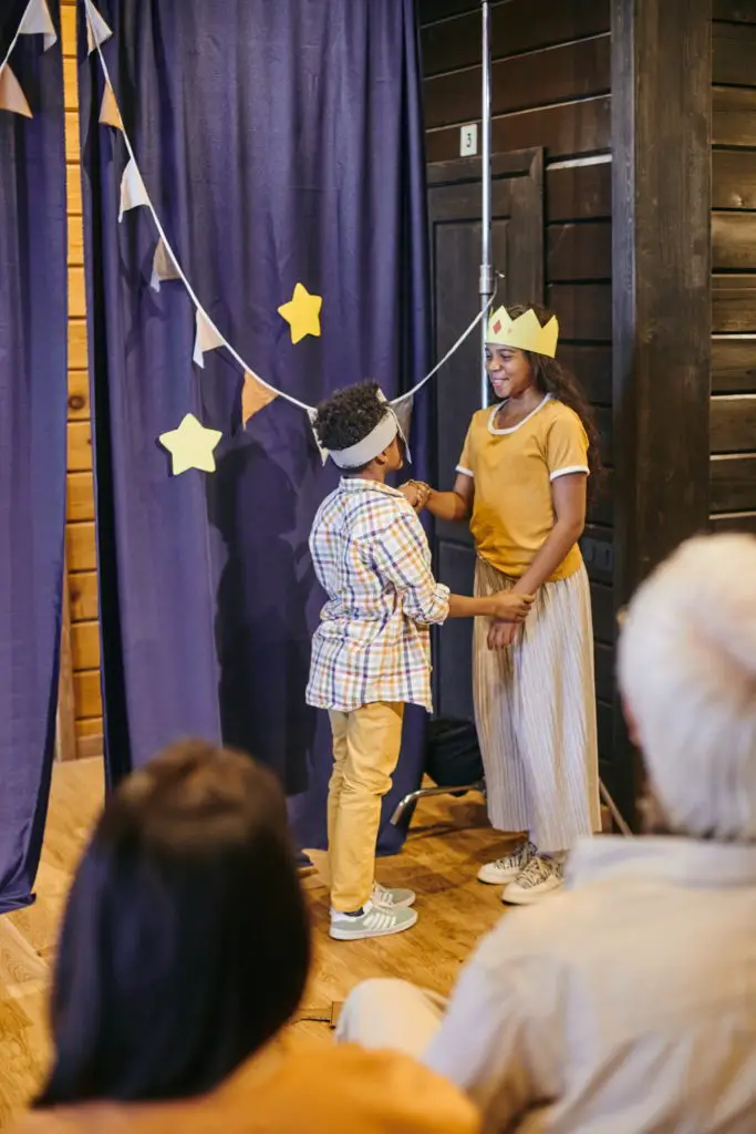 kids in costumes playing on stage of home theatre while standing by blue curtains decorated with handmade stars