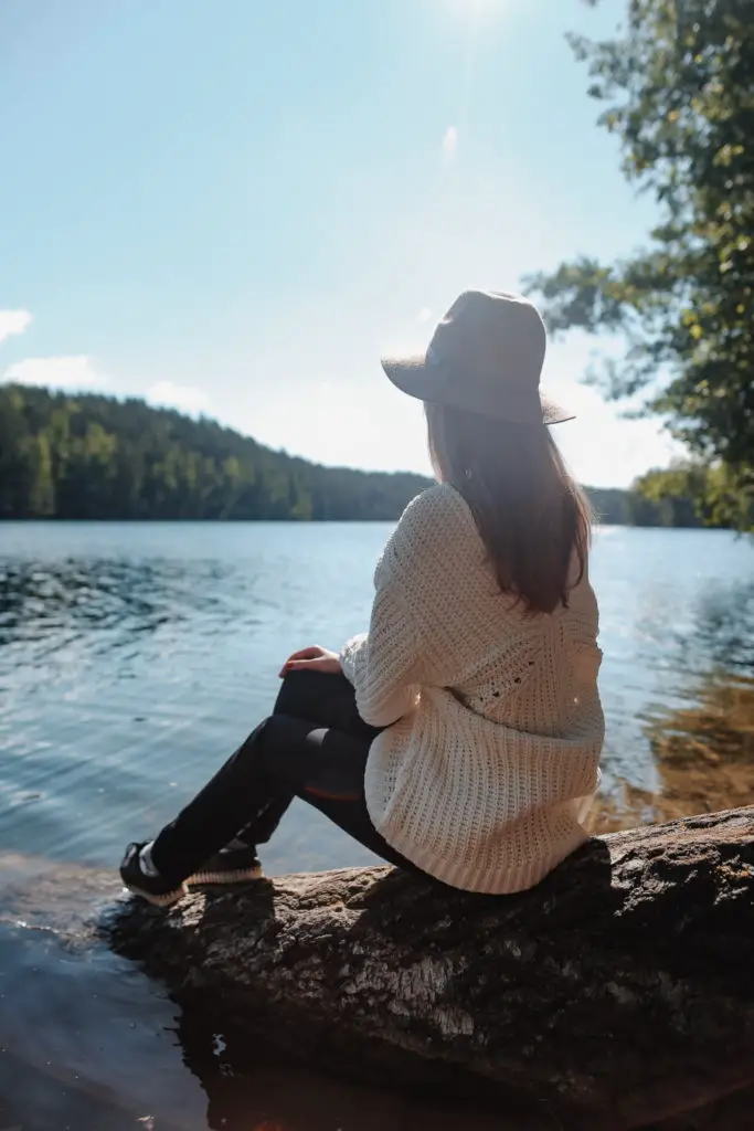 Back view of a woman sitting in the sunshine on a rock beside a lake