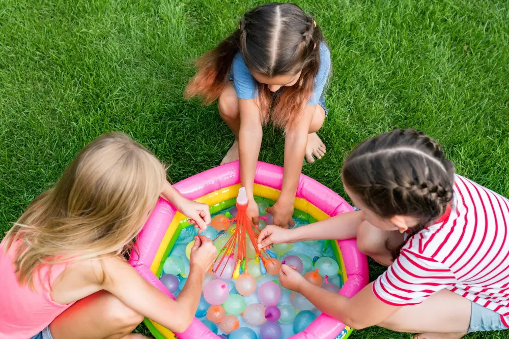 3 kids sitting around a small pool full of little water balloons