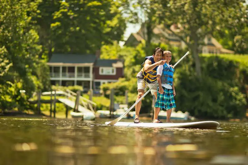 Father teaching his sun to paddleboard on a lake near their lake house