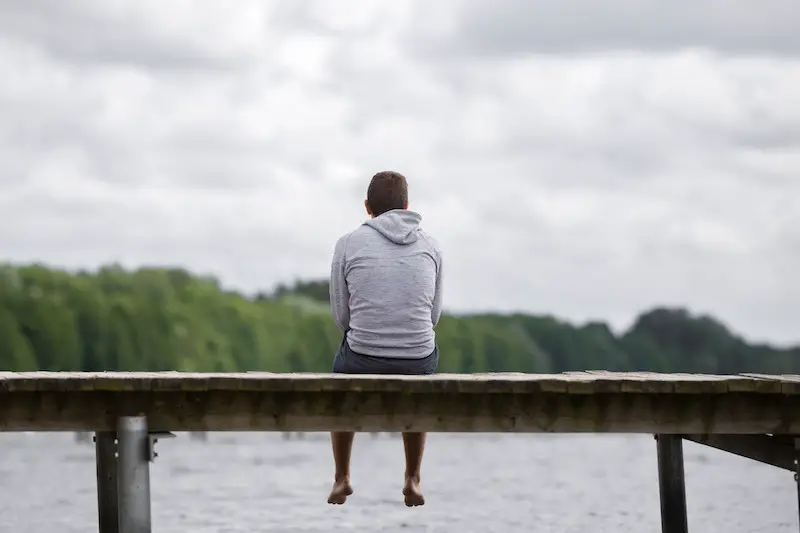 Young man sitting on a pontoon near a beautiful lake listening to the sounds 